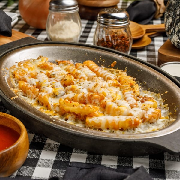 Pete's Pizza cheesy fries in a cast iron pan, with parmesan and chili flakes in the background.