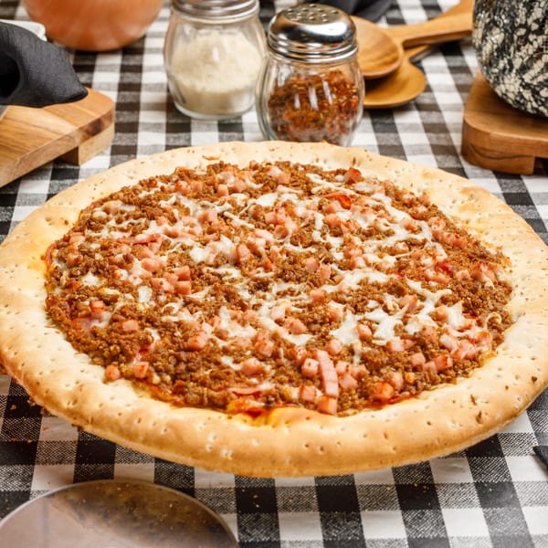 A Pete's Pizza with ground beef and ham, on a black and white checkered tablecloth.