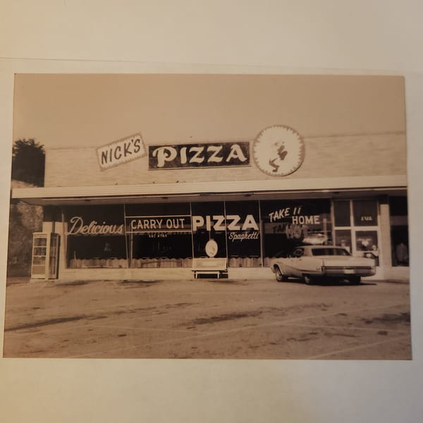 Sepia-toned vintage photo of Nick's Pizza storefront with a car parked outside.