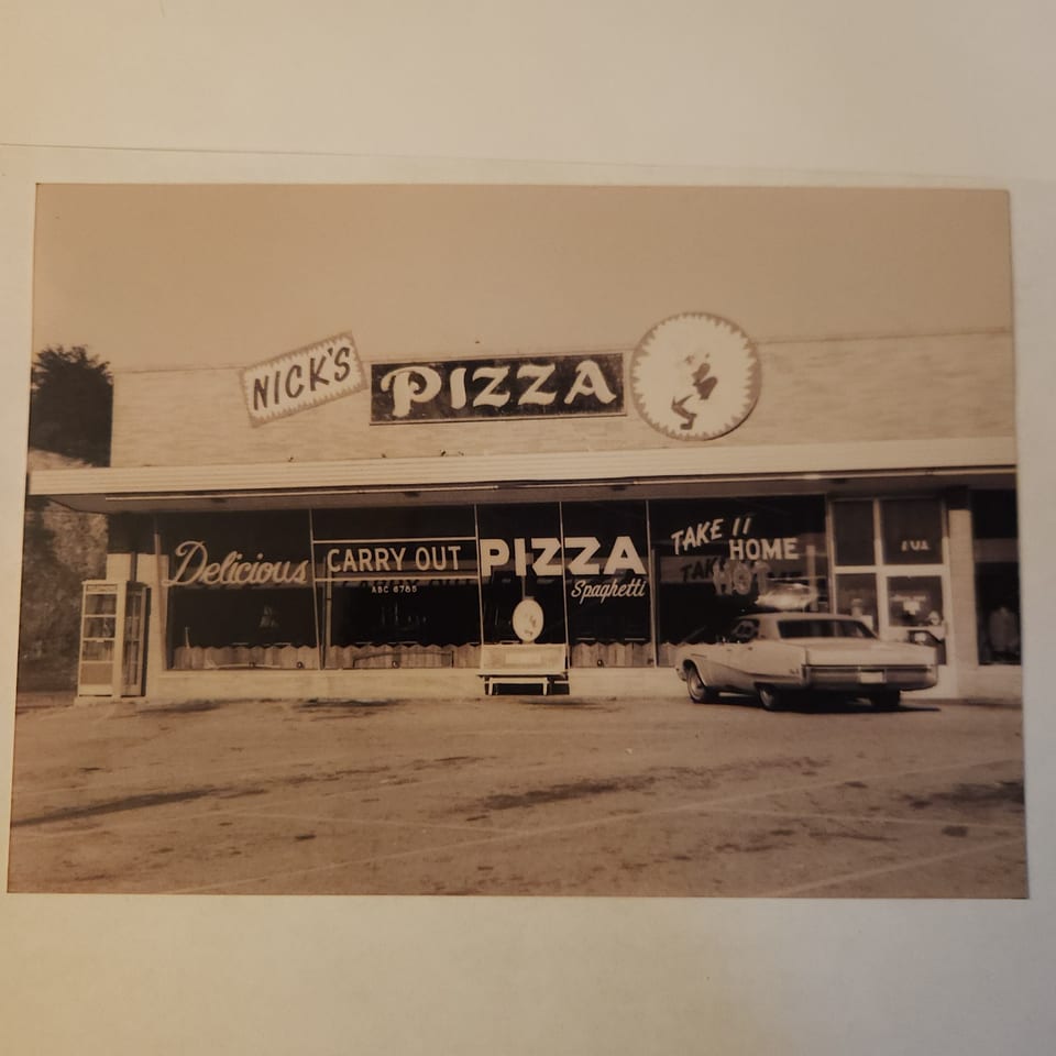 Sepia-toned vintage photo of Nick's Pizza storefront with a car parked outside.