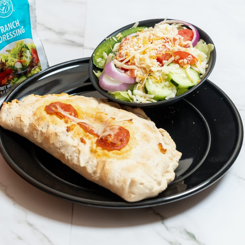 A pepperoni calzone and a side salad with ranch dressing on a black plate.