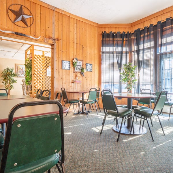 Pete's Pizza dining room with wood paneling, green chairs, round tables, and large windows.