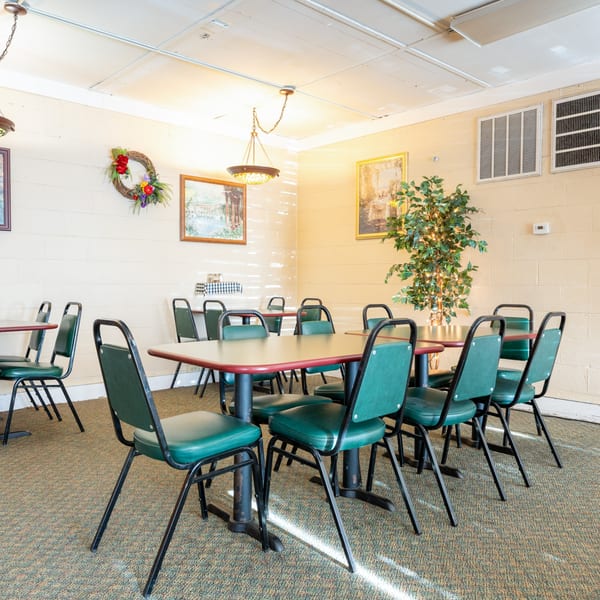 Empty dining room at Pete's Pizza with green chairs, red-edged tables, and light-colored walls.