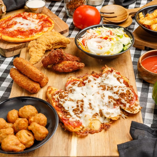 A feast of Pete's Pizza dishes, including pizzas, chicken tenders, wings, and sides on a checkered tablecloth.