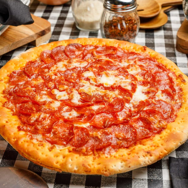 A whole pepperoni pizza from Pete's Pizza on a black and white checkered tablecloth.