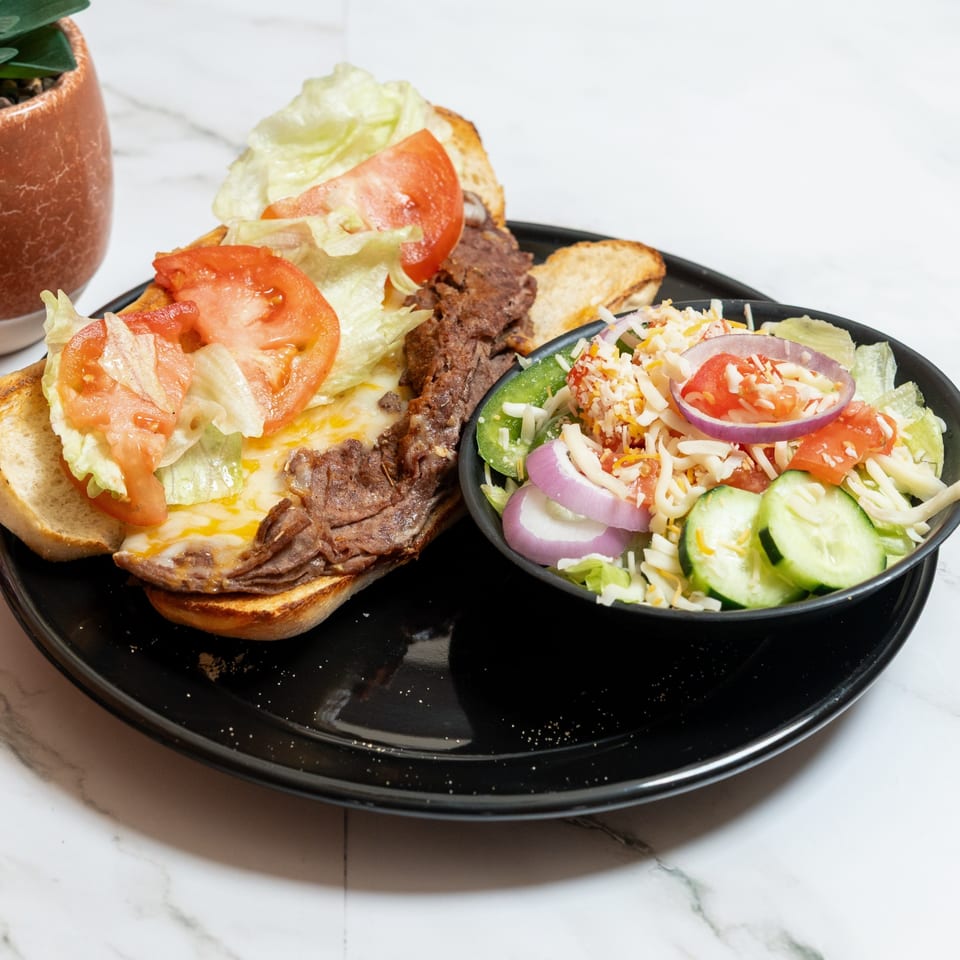A Pete's Pizza sandwich with melted cheese, lettuce, and tomatoes, served with a side salad.