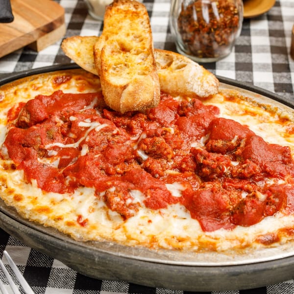 Pete's Pizza's baked pasta dish with melted cheese, rich red sauce, and toasted bread on a checkered tablecloth.