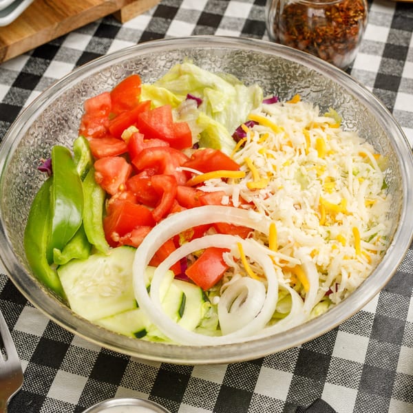 A fresh garden salad with lettuce, tomatoes, green peppers, cucumbers, onions, and shredded cheese.