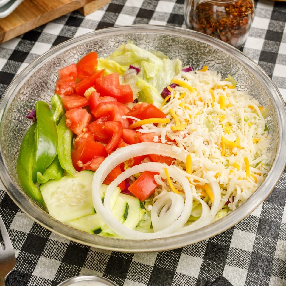 A fresh garden salad with lettuce, tomatoes, green peppers, cucumbers, onions, and shredded cheese.