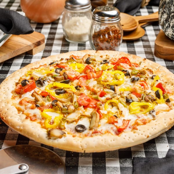Pete's Pizza with colorful toppings, including yellow peppers, tomatoes, olives, and mushrooms on a checkered tablecloth.