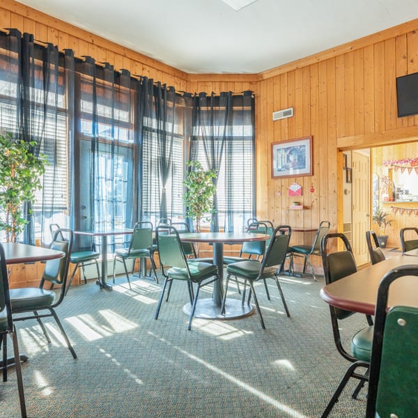 Pete's Pizza dining room with wood-paneled walls, black curtains, and green and black chairs at round tables.