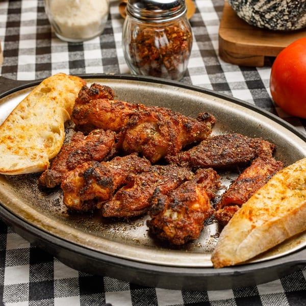Pete's Pizza's spicy chicken wings and toasted bread in a metal pan on a checkered tablecloth.
